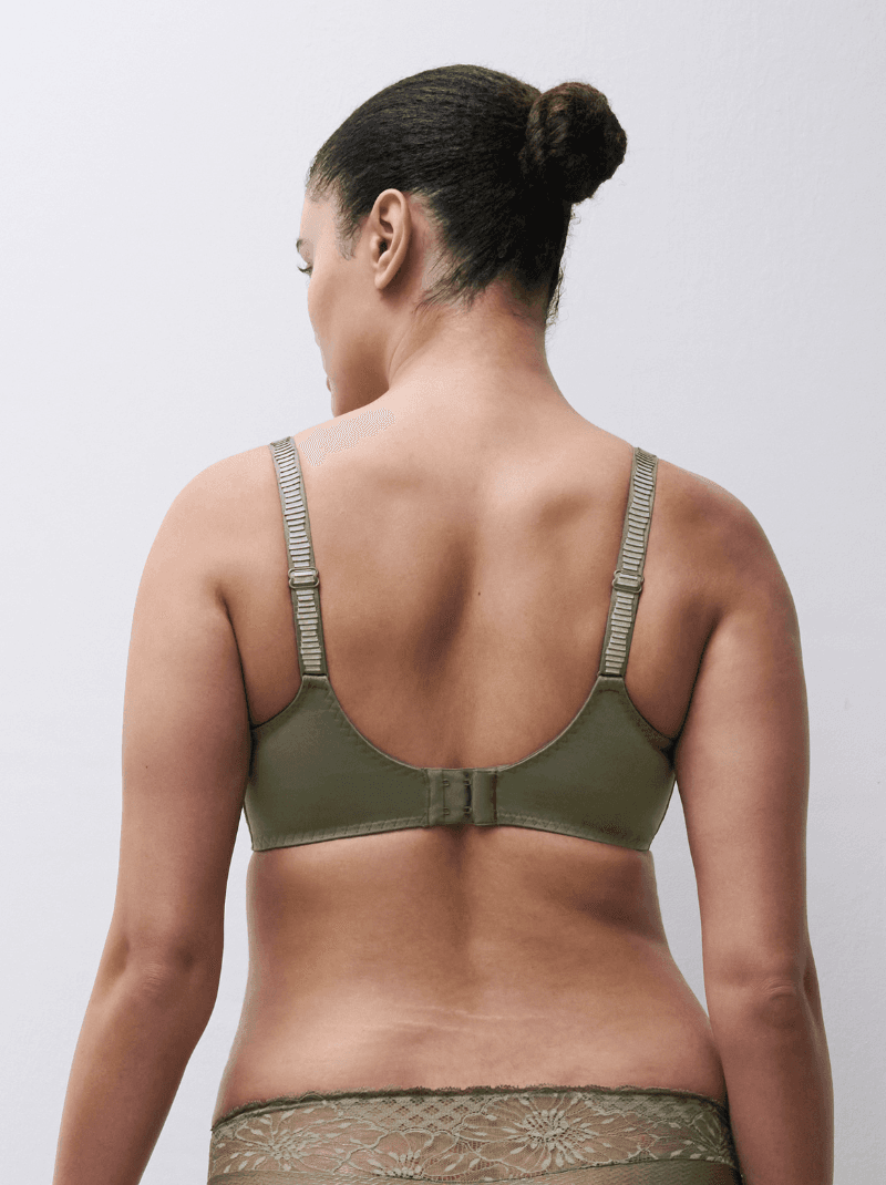 Rear view of a person wearing an olive green bra and lace-trimmed underwear, with hair in a bun against a neutral background.