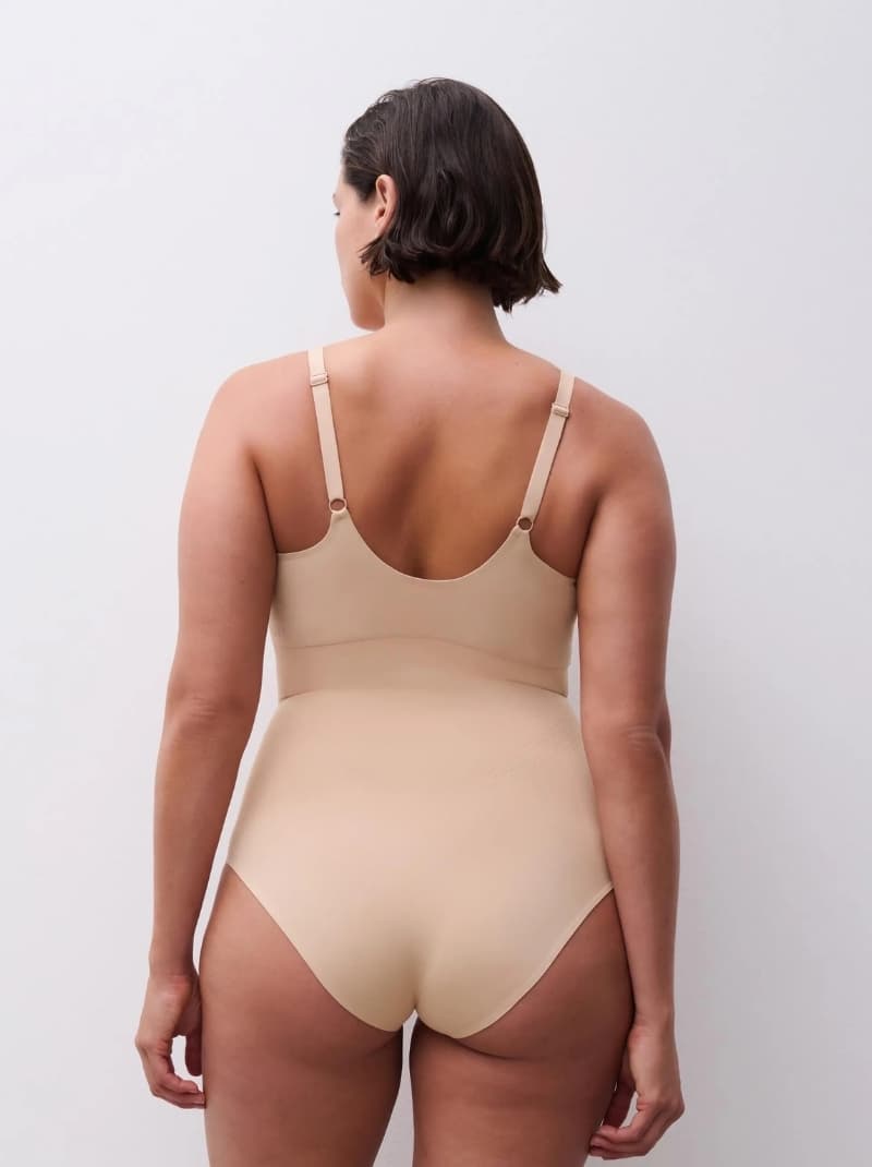 Back view of a person wearing a beige one-piece undergarment with adjustable straps, against a plain background.