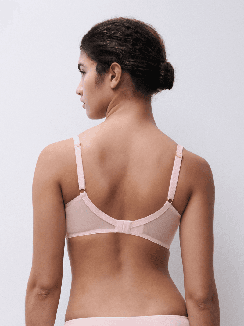 Woman with hair in a bun, seen from behind, wearing a light pink bra with adjustable straps against a plain white background.