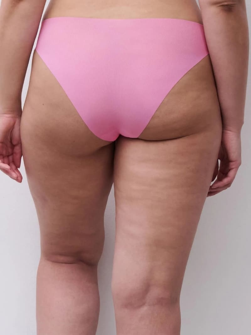 Rear view of a person wearing pink underwear, displaying natural skin texture and curves, standing against a neutral background.