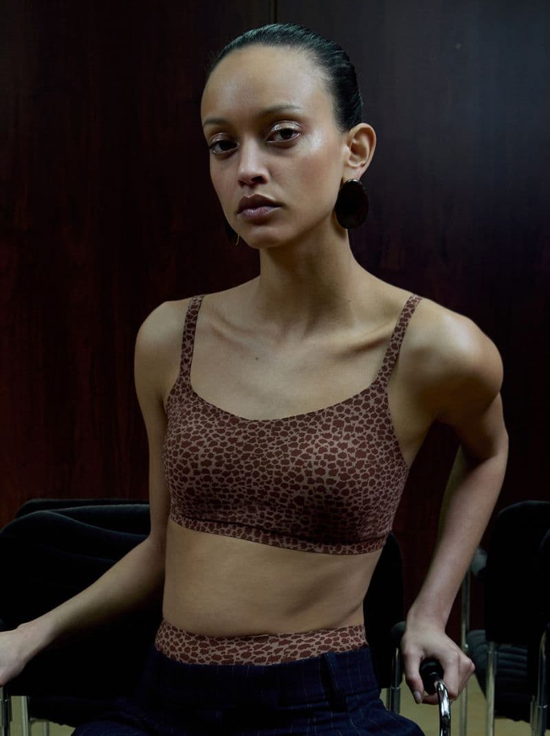 Person seated wearing a brown leopard-print top and earrings, against a dark wooden background.