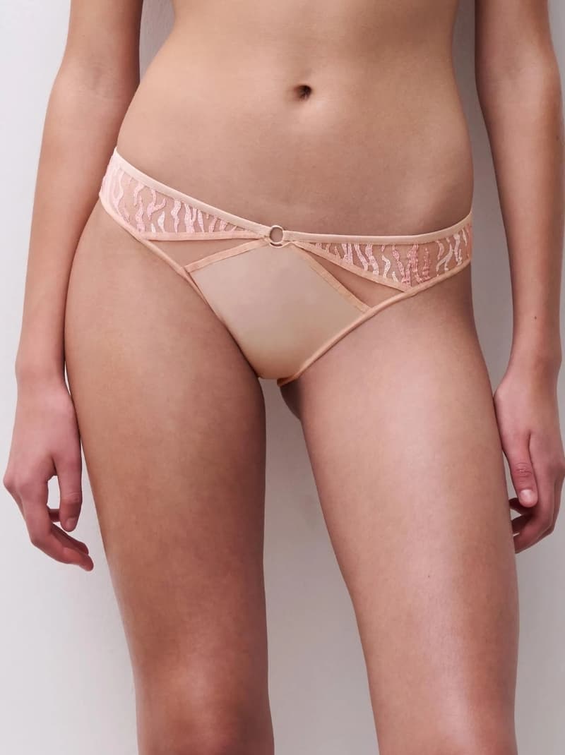 Close-up of a person wearing peach panties with lace detailing and a small ring accent at the front waistband.