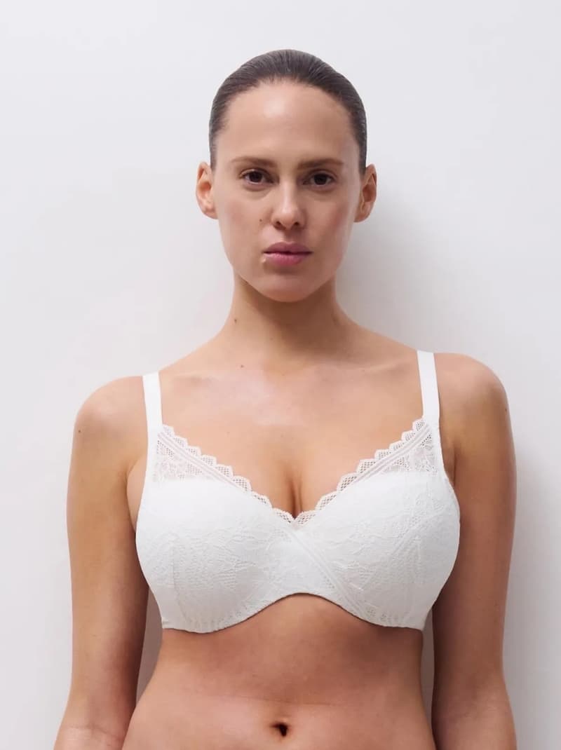 Woman wearing a white lace bra, standing against a plain white background.