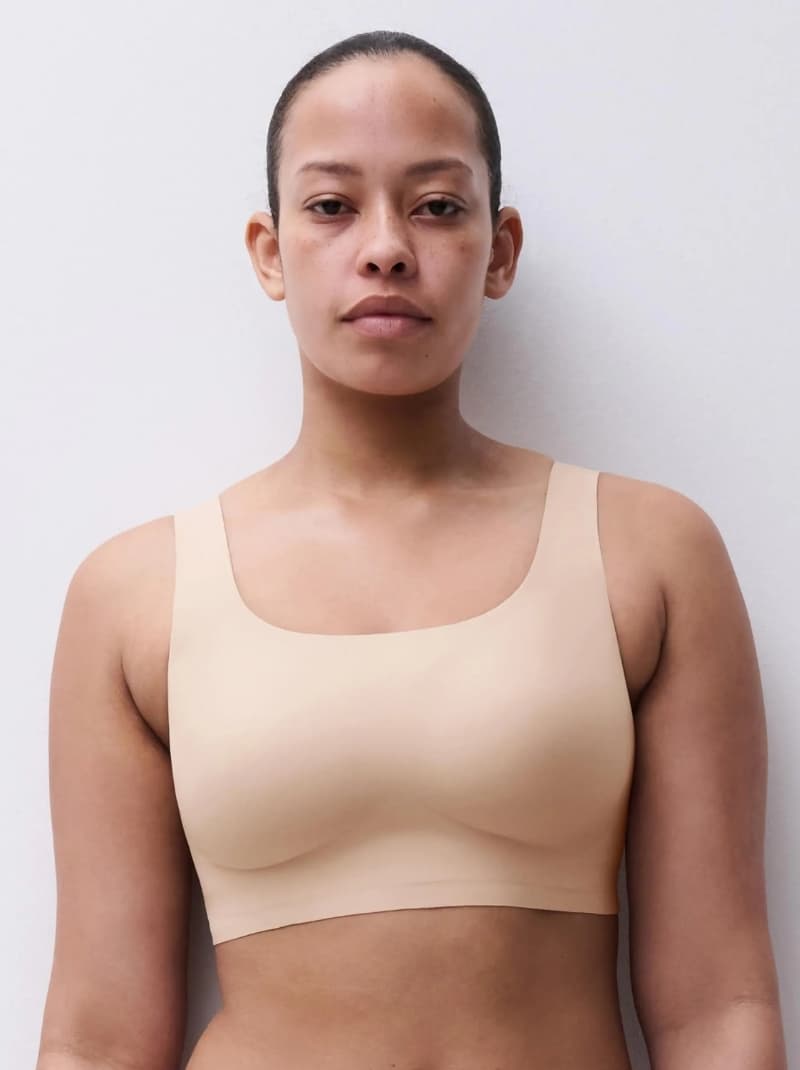 Person wearing a beige bra against a light background, looking directly at the camera.