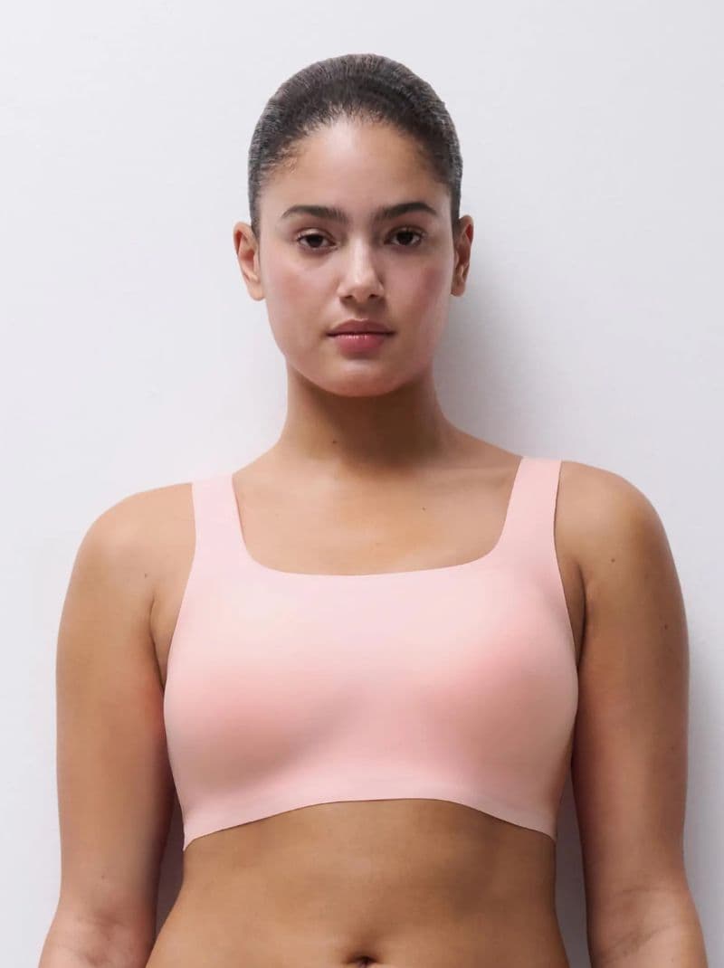 Person wearing a pink bra, standing against a plain white background, looking directly at the camera.