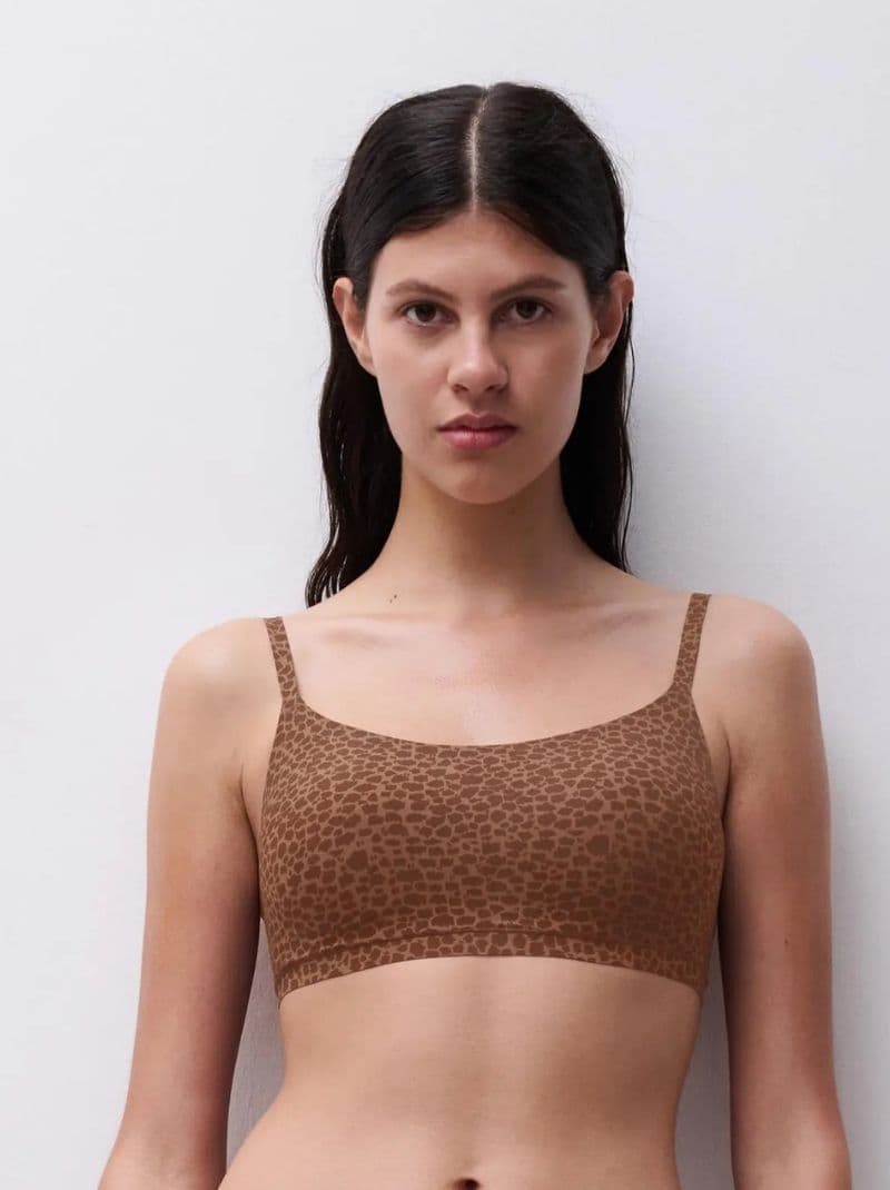 Person wearing a brown, leopard-print bralette, standing against a plain white background.