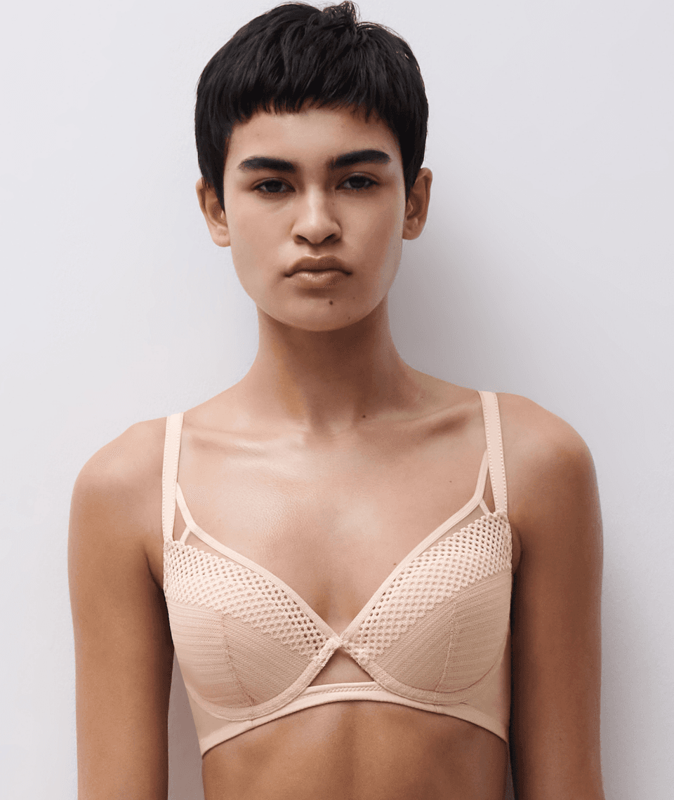 Person with short dark hair wearing a beige textured bra against a white background.