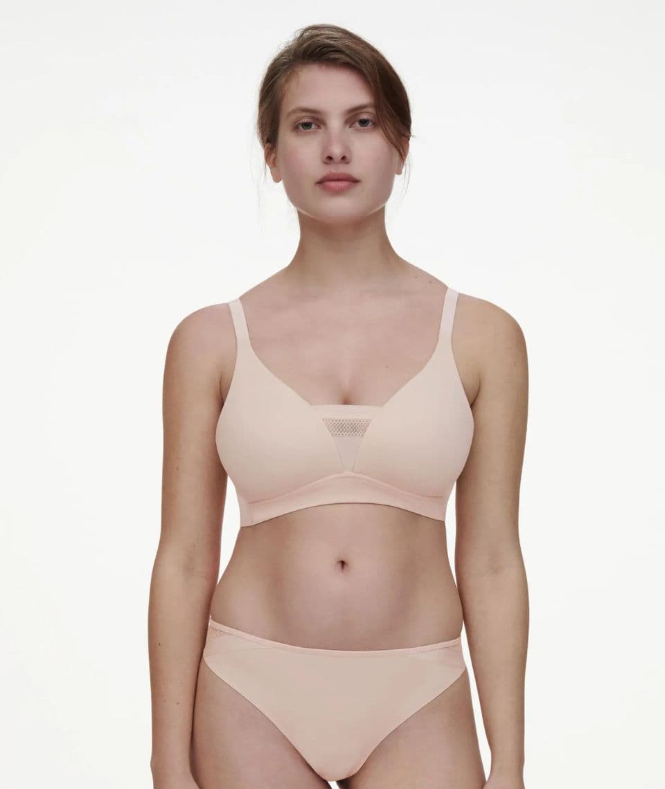 A woman is wearing a beige bra and panties set, standing against a plain white background.