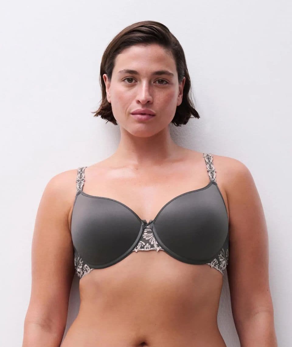 Person wearing a gray bra with floral strap details, standing against a plain white background.