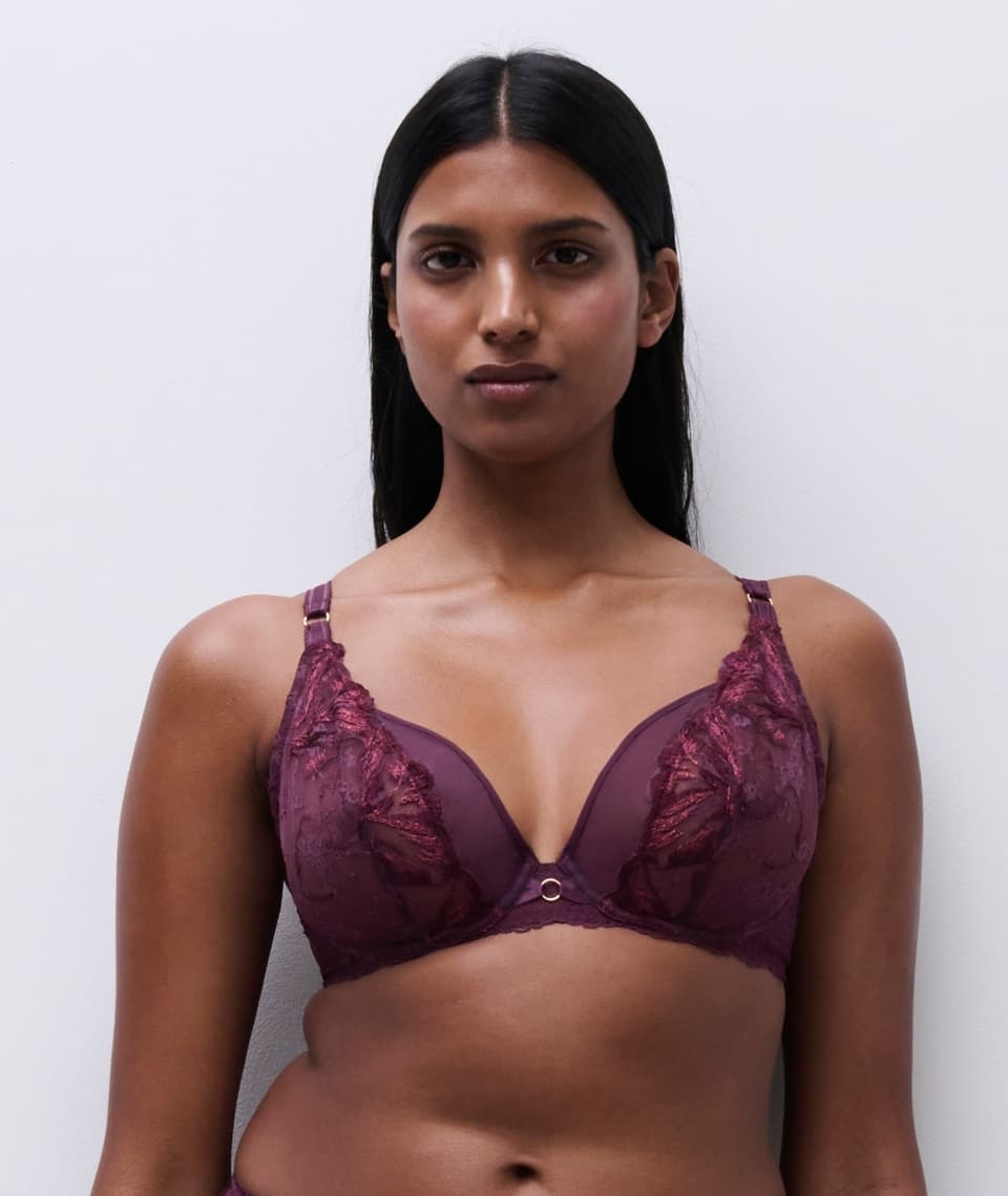 Woman wearing a maroon lace bra standing against a plain white background.