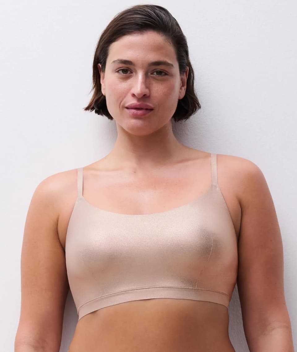 A woman with short brown hair wearing a golden bra stands against a plain white background.