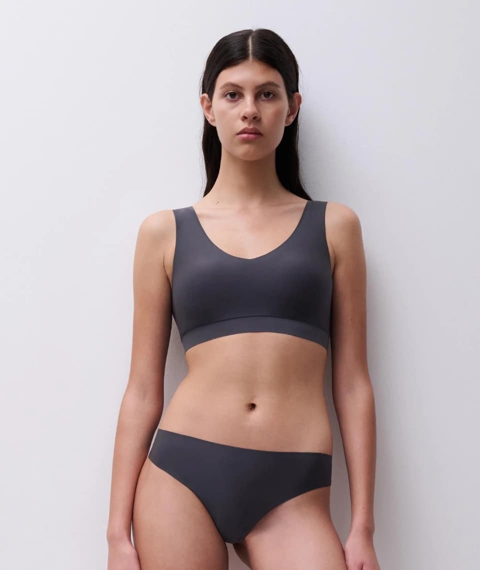Person wearing a gray bralette and underwear, standing against a plain white background.