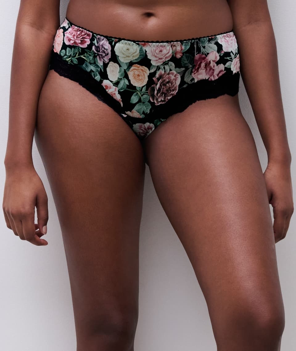 Person wearing floral print underwear with black lace trim, standing against a plain background.