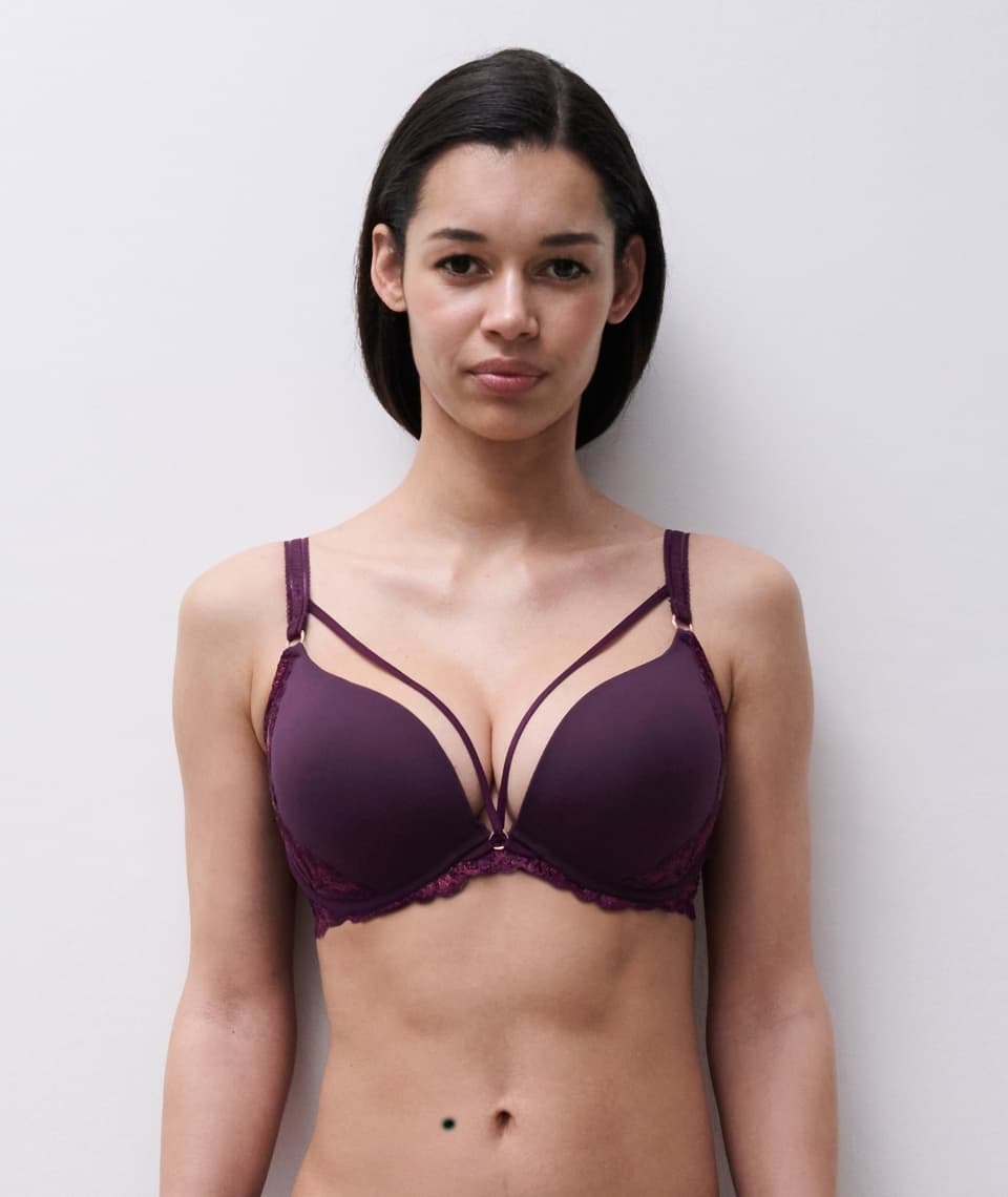 Person wearing a dark bra with strappy details, standing against a plain white background.
