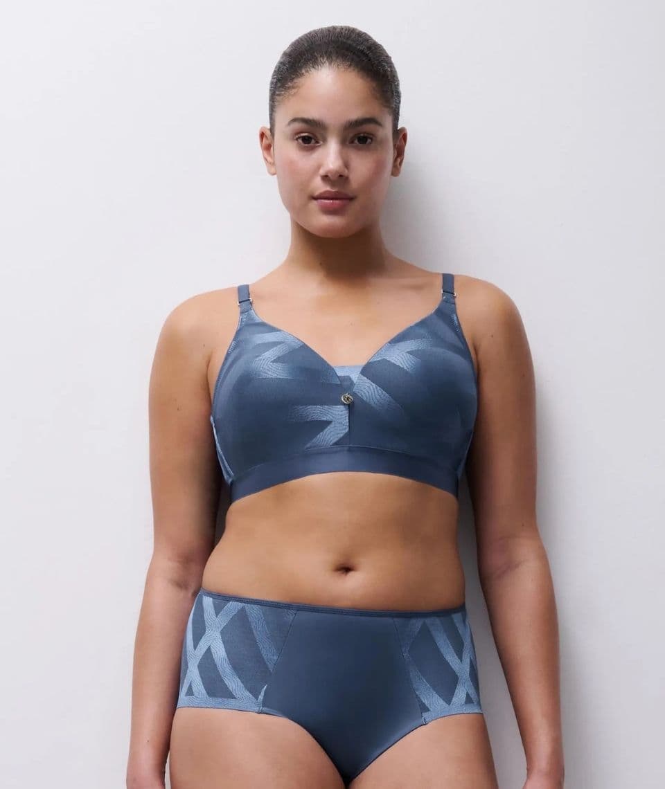 Person wearing a matching blue bra and panties set with geometric patterns, standing against a plain white background.