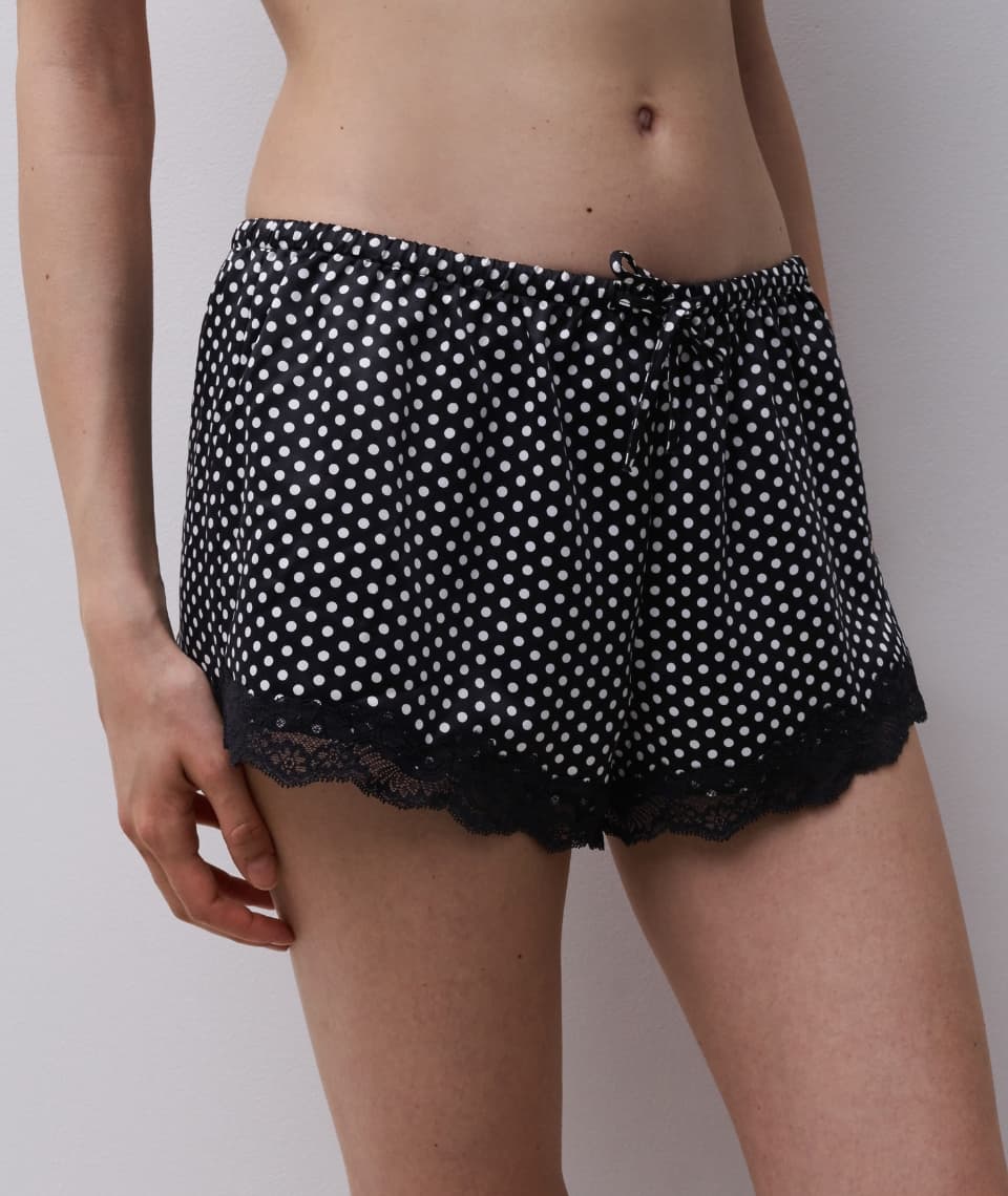 Person wearing black polka dot shorts with lace trim standing against a light gray wall.