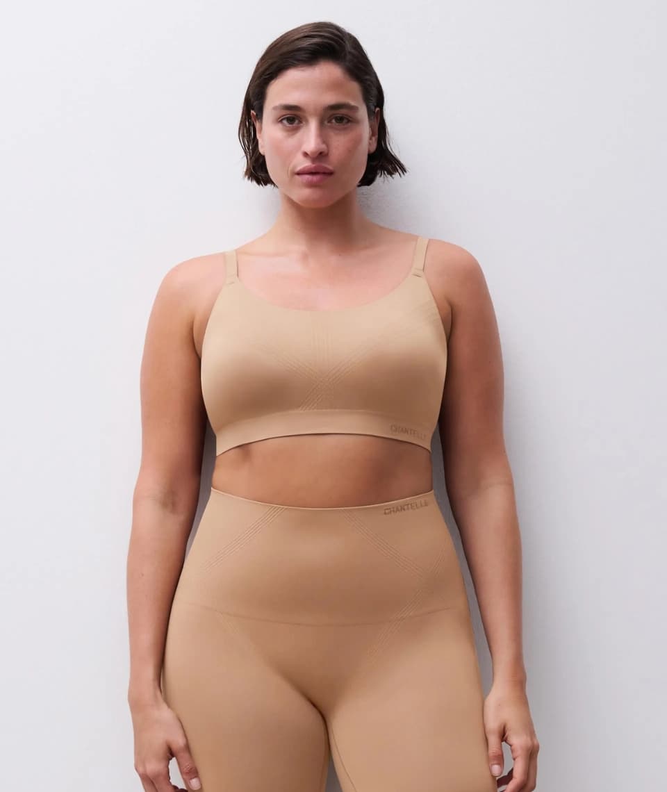 A person wearing a seamless tan-colored bra and leggings stands against a plain white background.