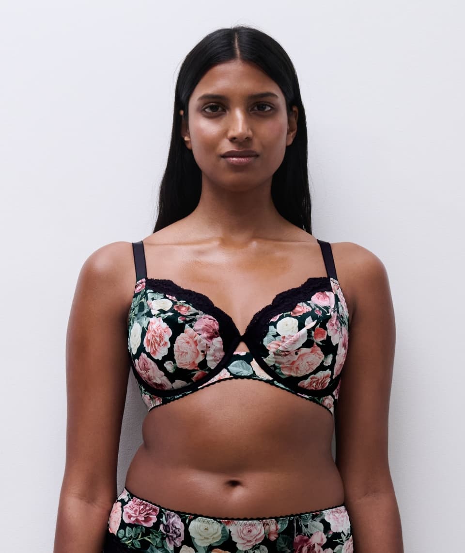 Person in floral lingerie set against a plain background, featuring a black base with pink and white flowers.