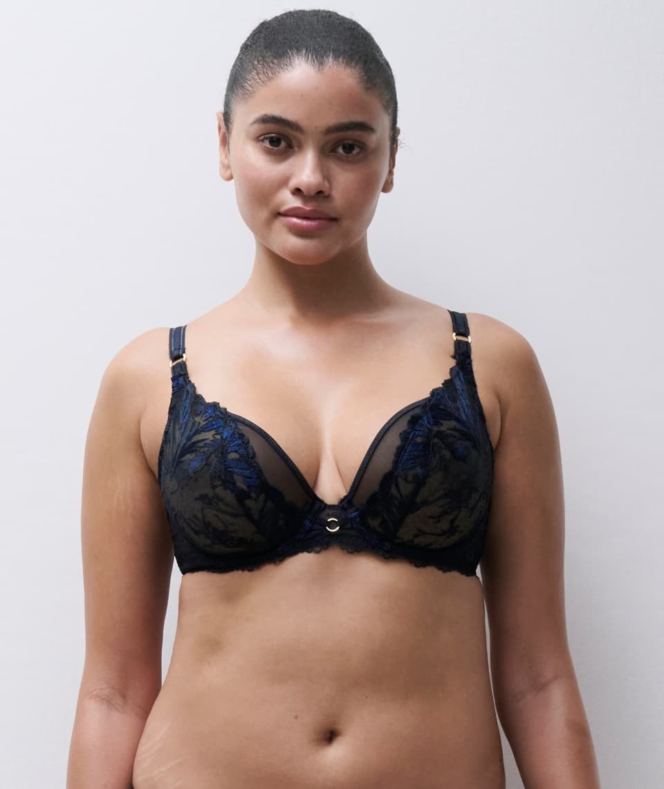 A person wearing a black lace bra with blue accents, standing against a plain background.