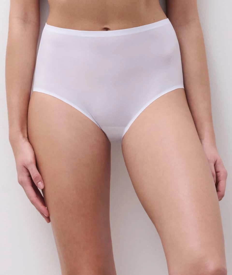 Person wearing white, high-waisted panties against a plain background, showing a close-up of the garment's fit and fabric.