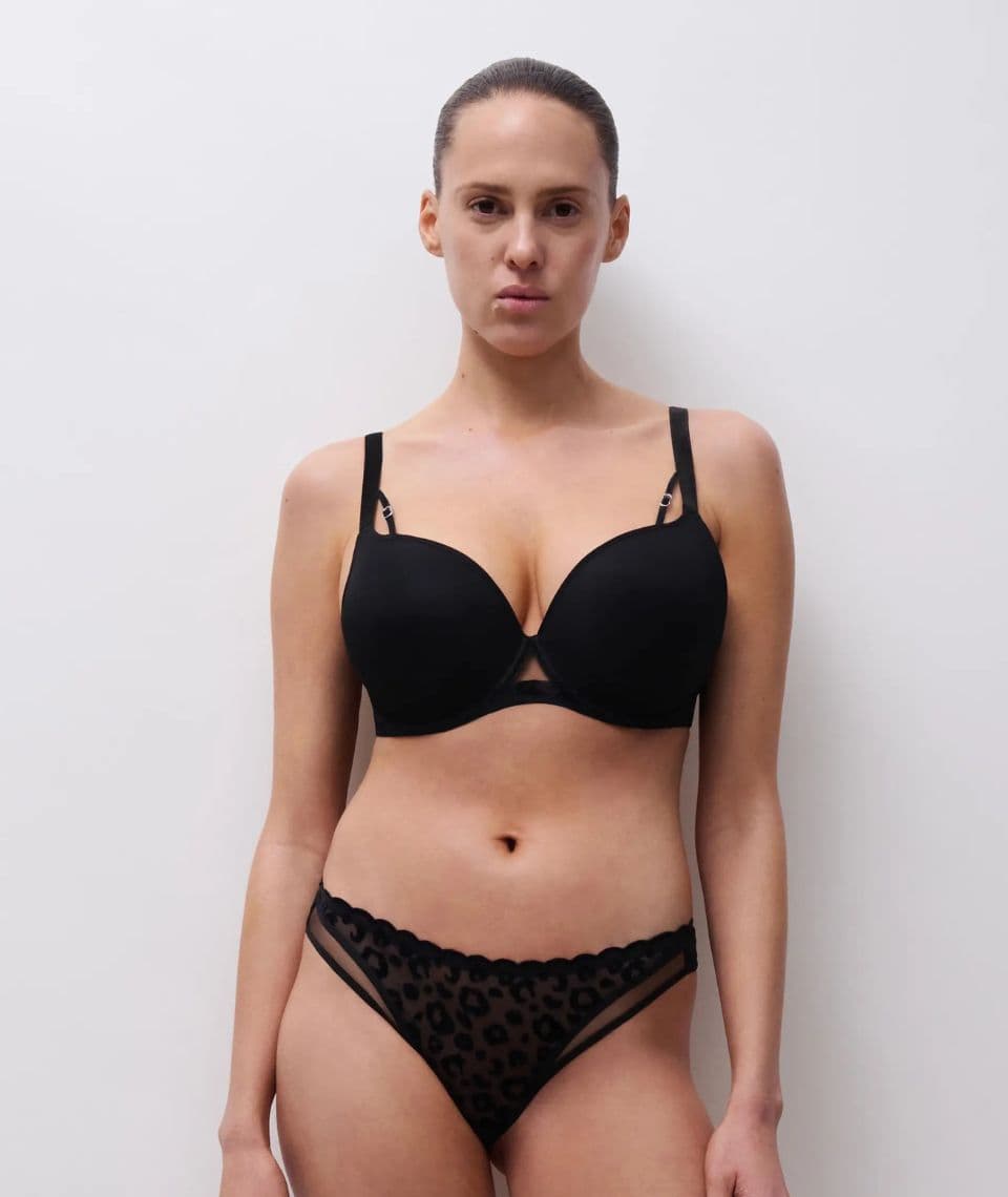 Person wearing a black bra and leopard print underwear stands against a plain white background.