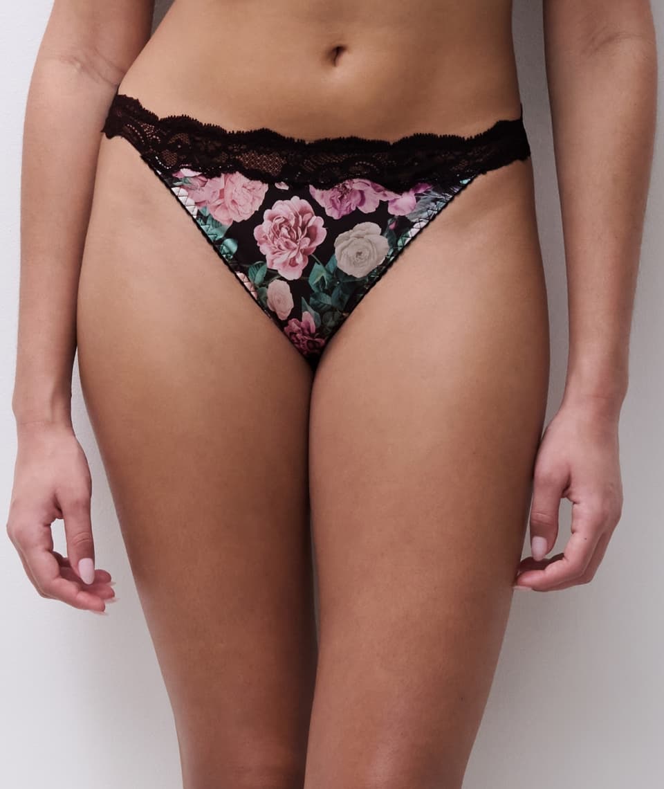 Woman wearing floral-patterned panties with black lace trim, standing against a plain background.