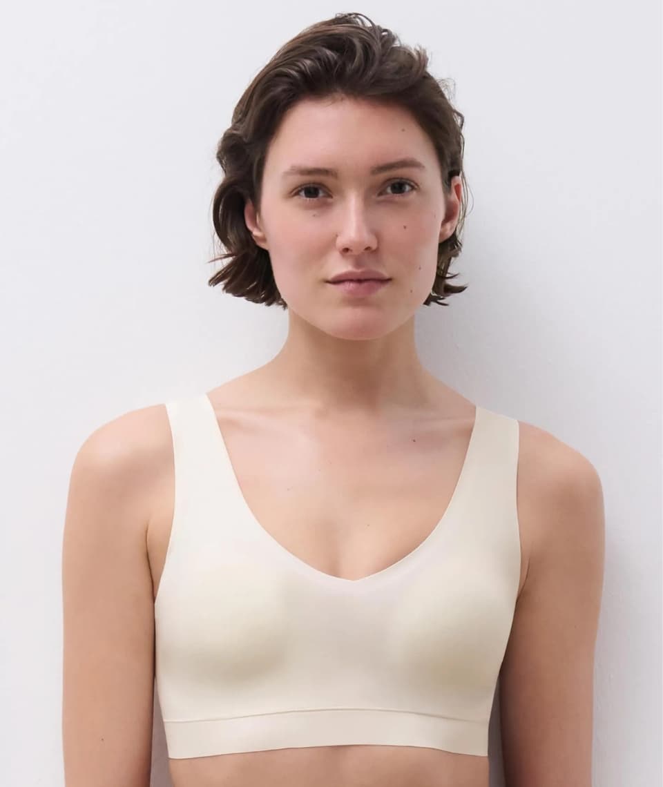 A person with short brown hair wearing a white bra, standing against a plain white background.