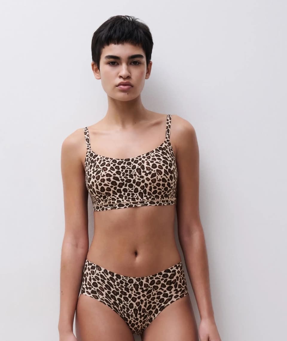Person wearing a leopard-print bralette and briefs set, standing against a plain white background.