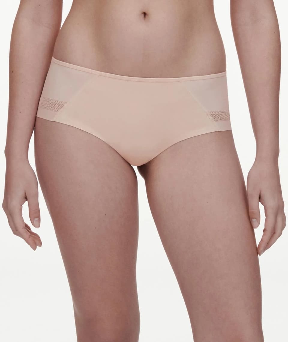 A person wearing a golden beige-colored seamless underwear with mesh side panels, standing against a white background.
