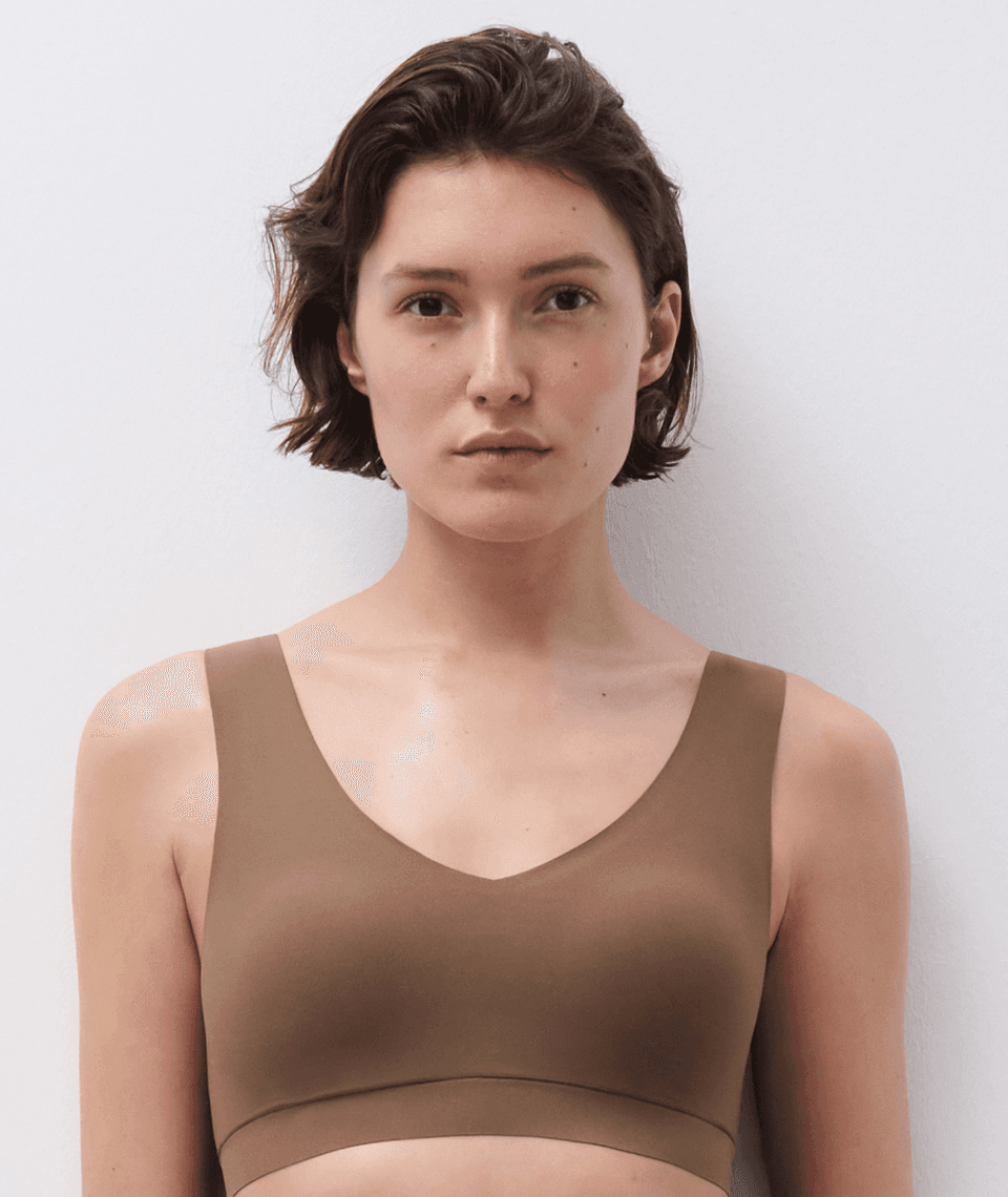 Person with short hair wearing a brown tank top, standing against a light background.