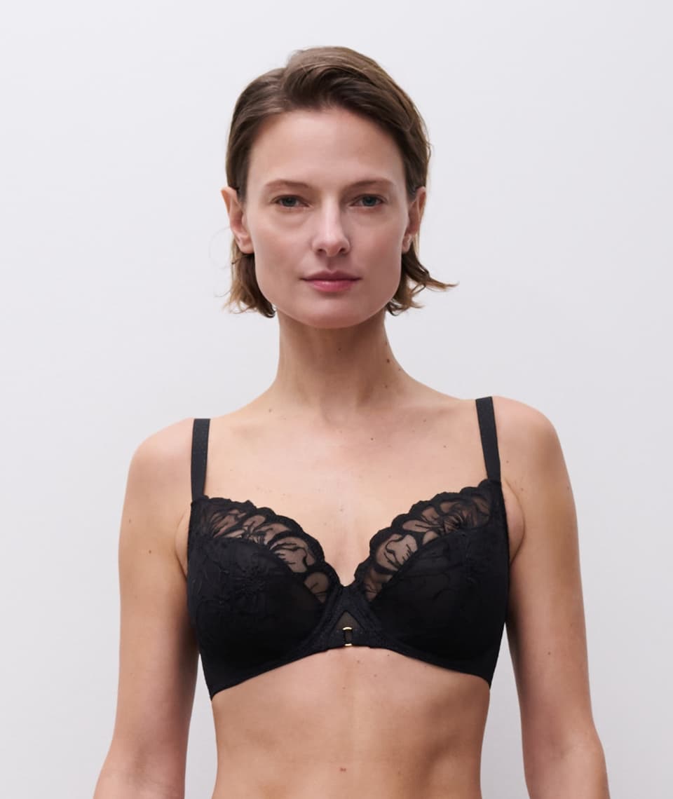 A person ina blacl lace bra, infront of a grey wall