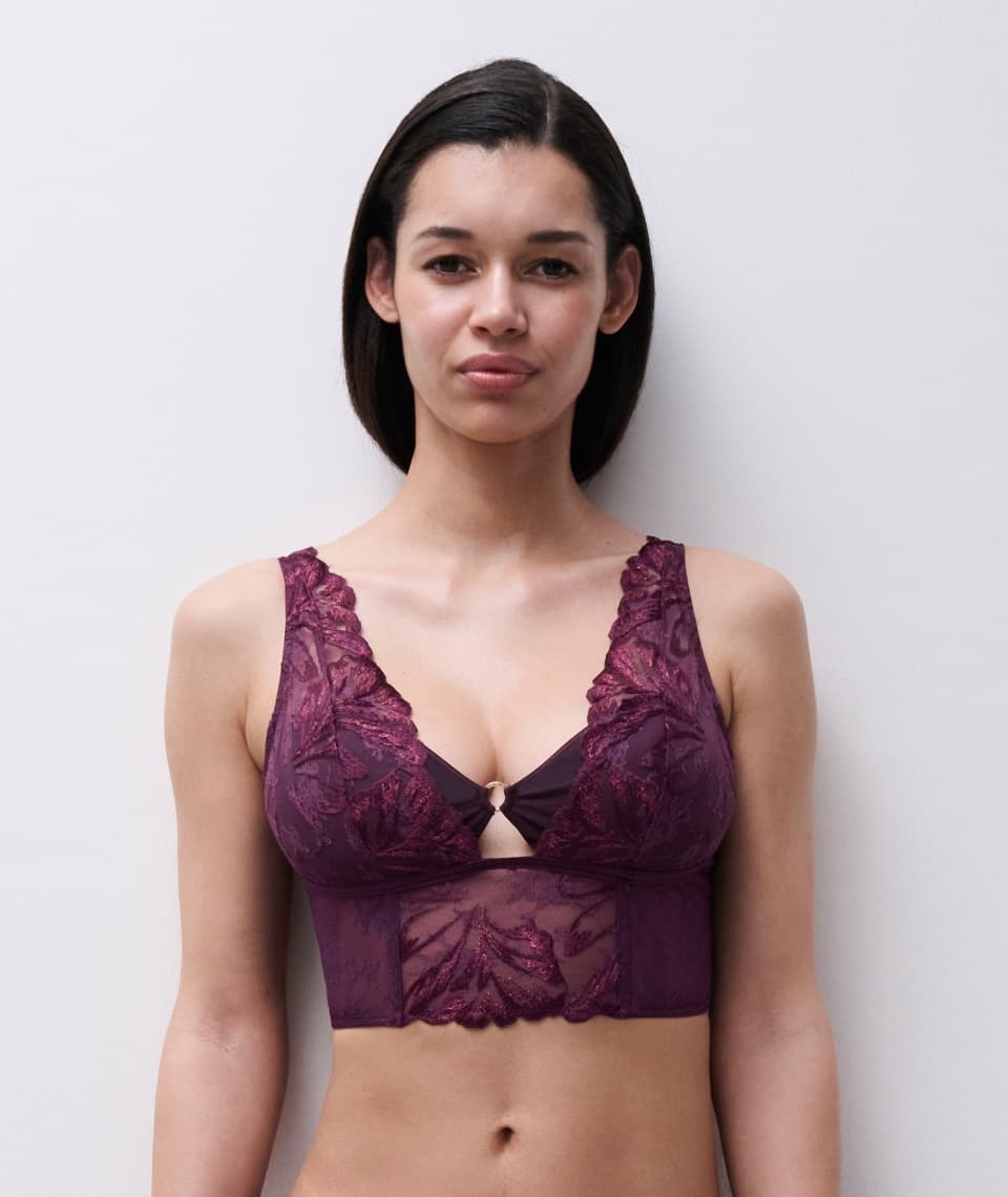 Person wearing a purple lace bralette with floral patterns, posing against a light gray background.