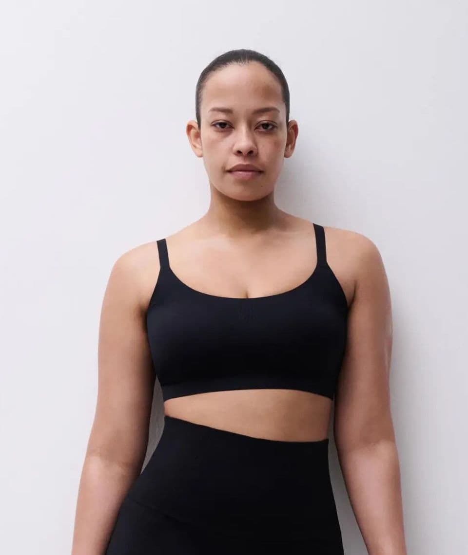Person in a black shapewear bra and leggings against a plain white background, facing forward with a neutral expression.