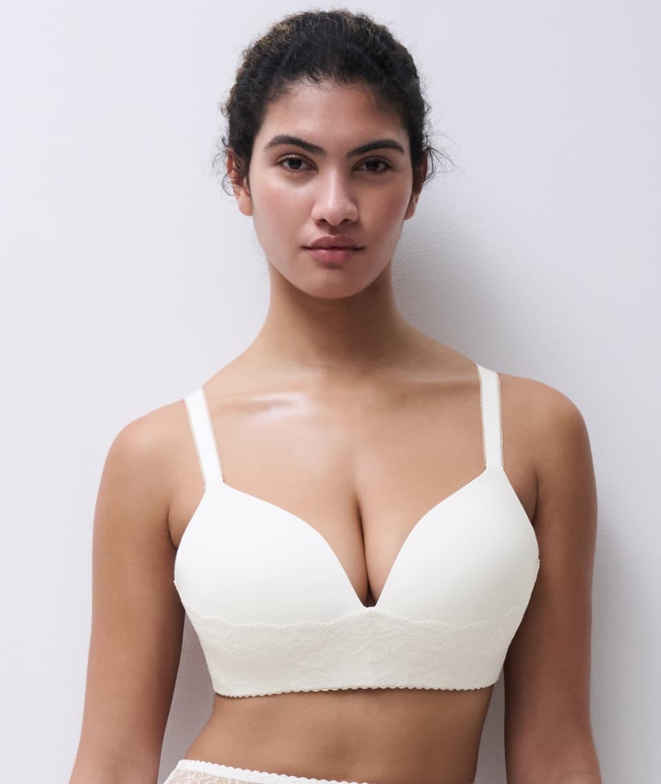 Person wearing a cream-colored bra with lace details, standing against a plain background.