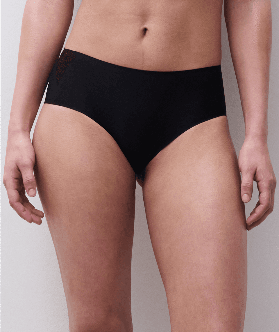 A person wearing high-waisted black underwear, shown from the waist to mid-thigh, standing against a light background.