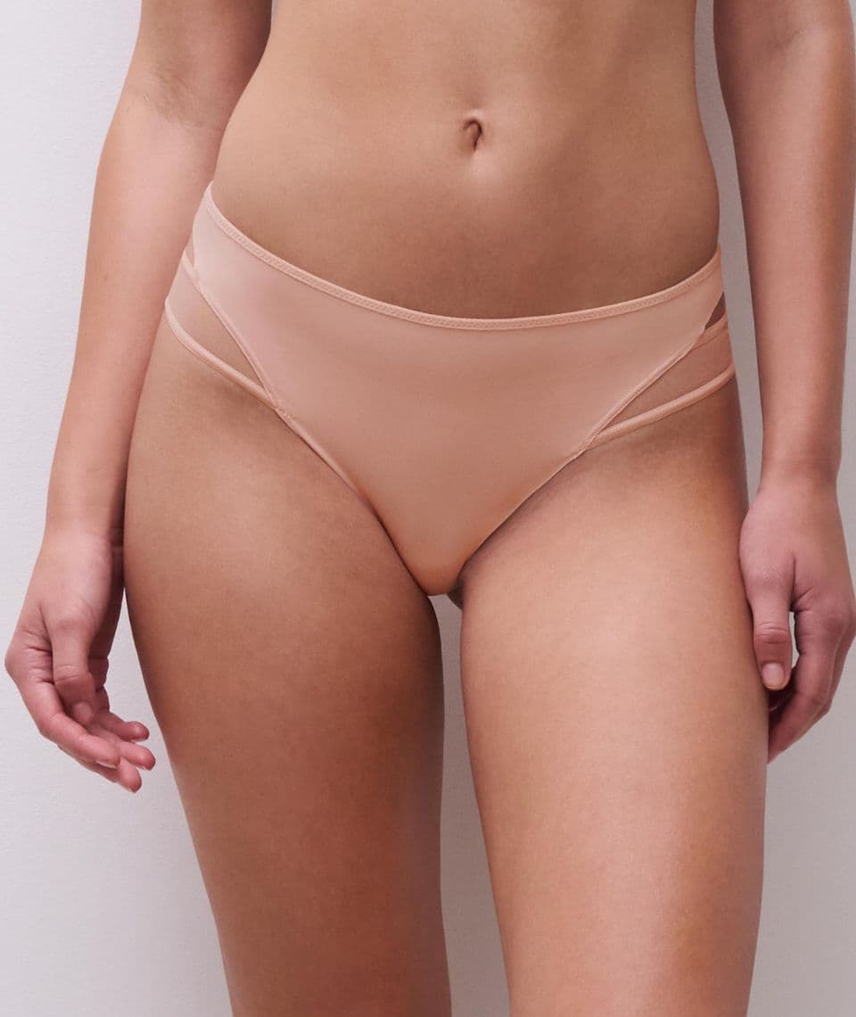 A person wearing light peach-colored bikini bottoms with a double strap detail against a plain white background.