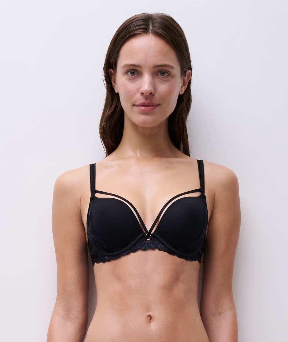 Person wearing a black lingerie bra, standing against a plain white background, looking forward.