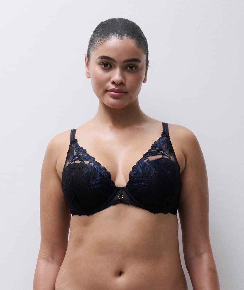 Person wearing a black lace bra with floral patterns, standing against a plain background.
