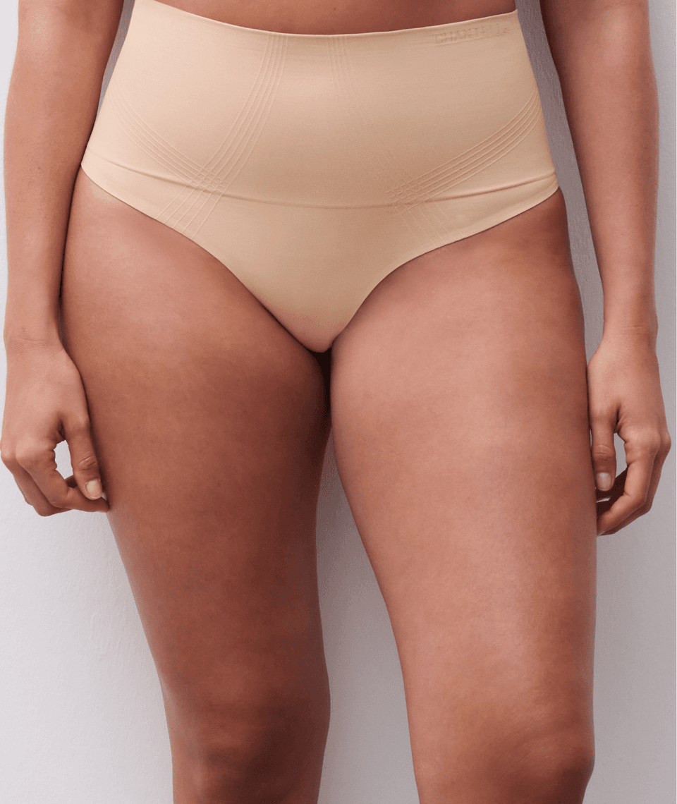 A person wearing high-waisted, skin-toned underwear, standing against a light background.