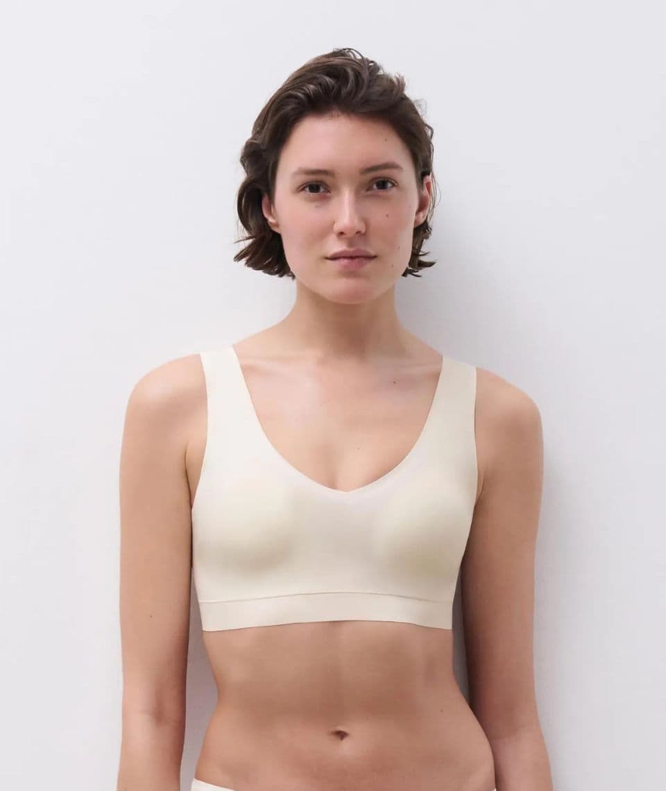 A person with short hair is wearing a white colored bra, standing against a plain white background.