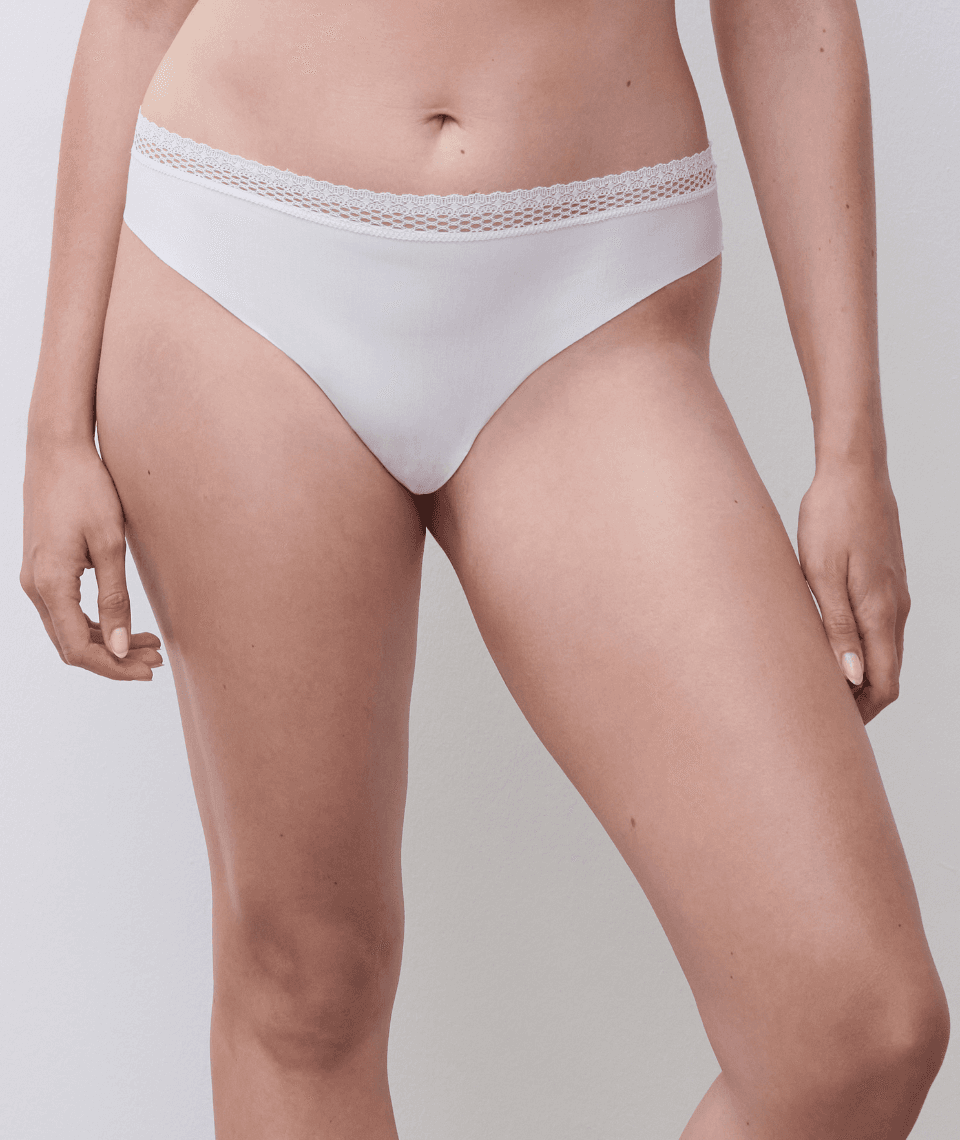 A person wearing white underwear with a lace waistband, standing against a plain background.