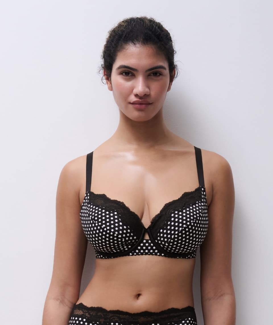 Person wearing a black and white polka dot bra with lace trim, standing against a plain white background.