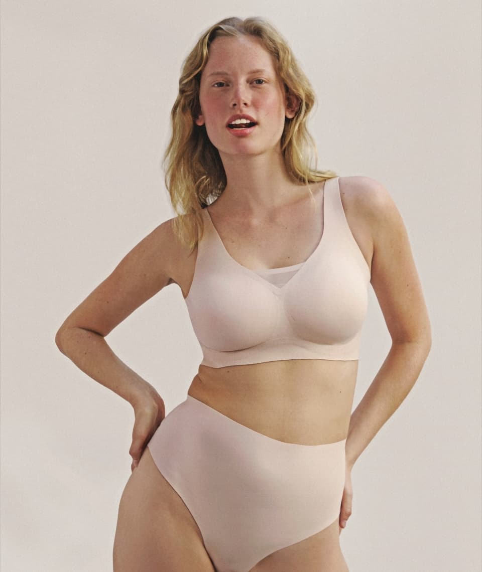 Person wearing a light pink underwear set, standing confidently with one hand on hip against a plain background.