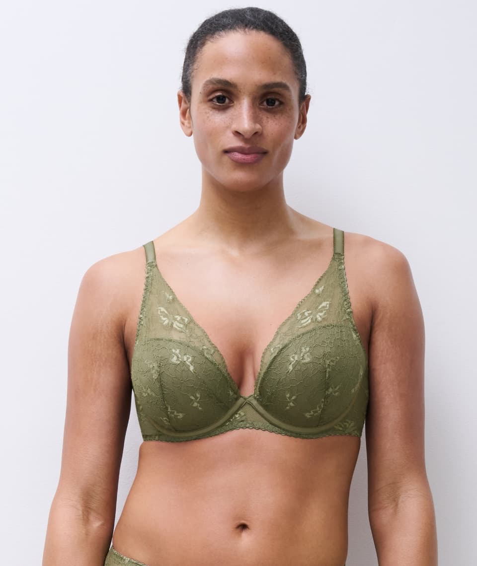 A person wearing a green lace bra stands against a plain white background, looking directly at the camera.