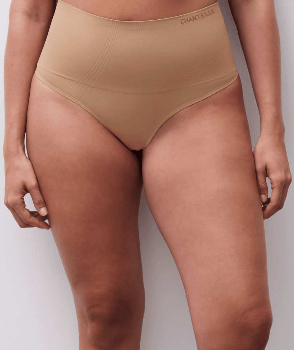 A person wearing high-waisted, beige shapewear briefs.