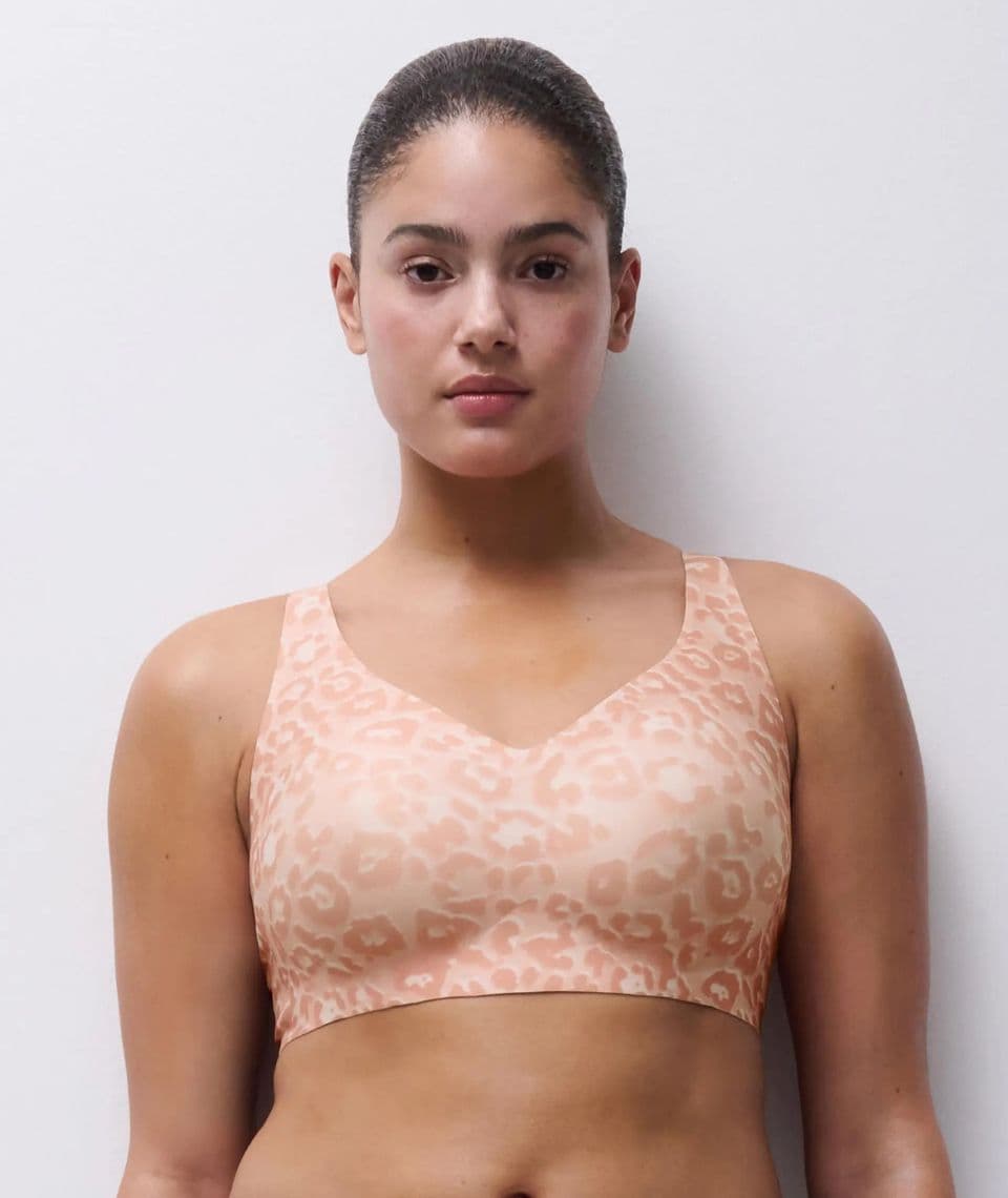 Person wearing a blush colored leopard-print bra with a neutral expression, standing against a plain white background.