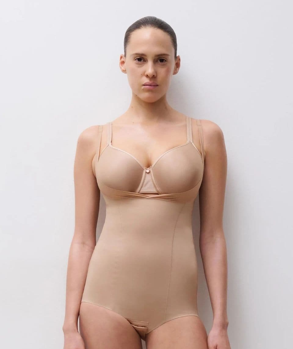 Person wearing a beige shapewear bodysuit against a white background, looking directly at the camera.