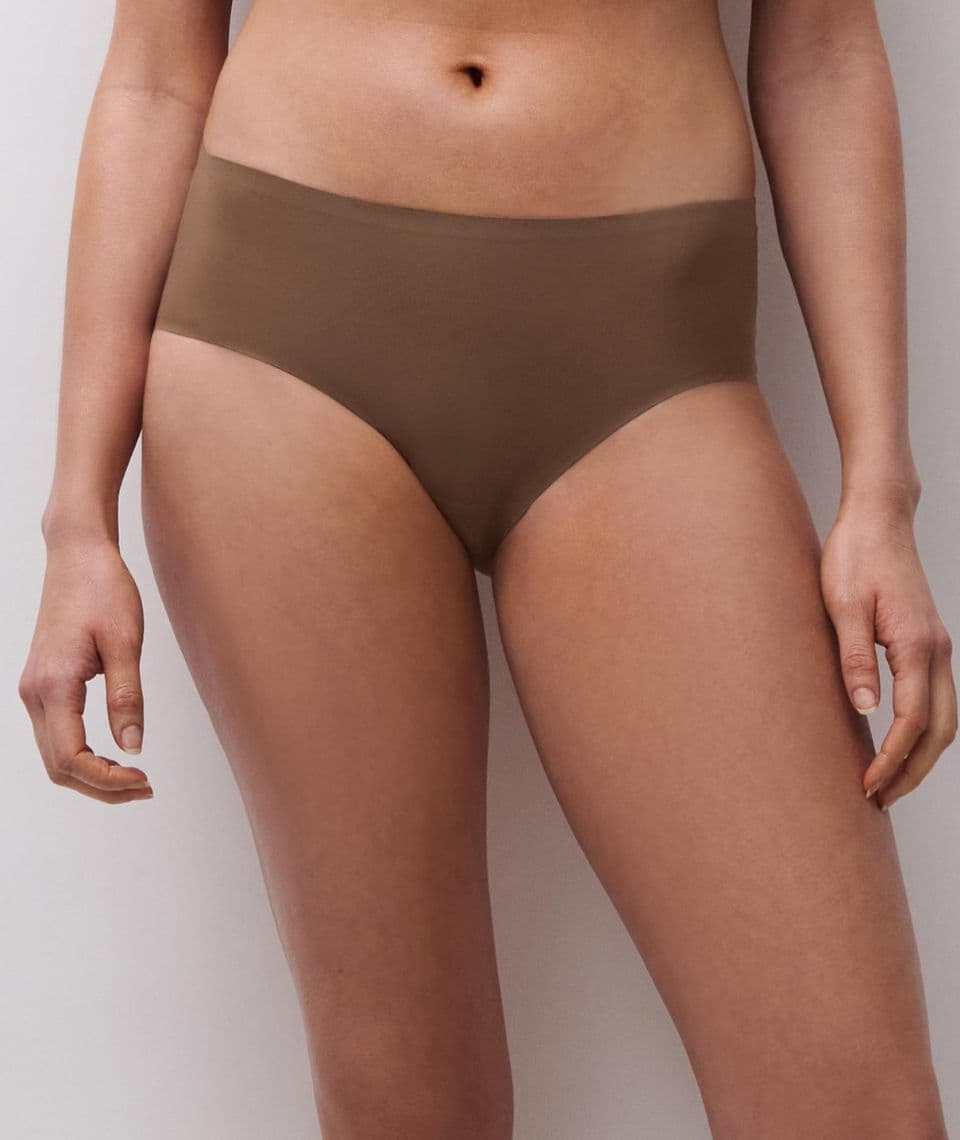 A person wearing high-waisted, seamless brown underwear, standing against a neutral background.