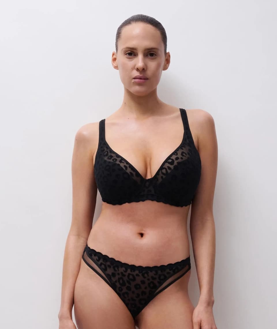 A person wearing a black leopard-print lingerie set, standing against a plain white background.