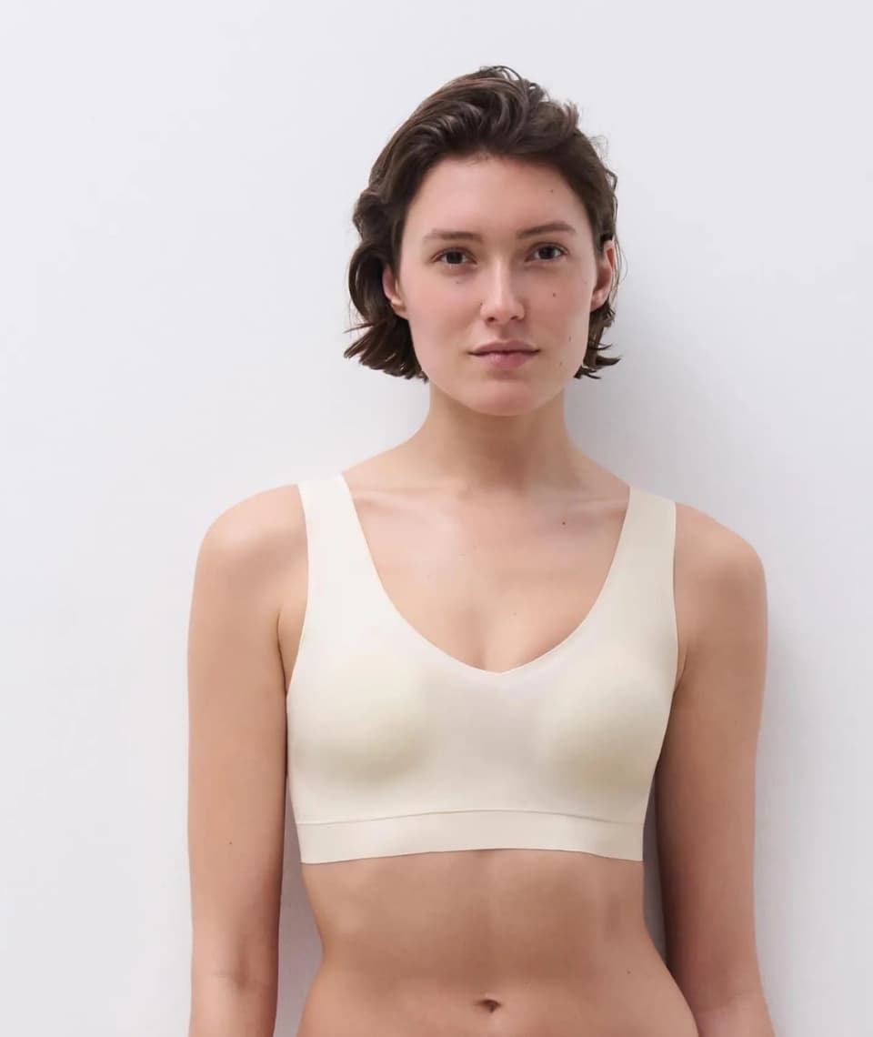 Person wearing a seamless bra, standing against a light gray background. The bra features wide straps and a scoop neckline.